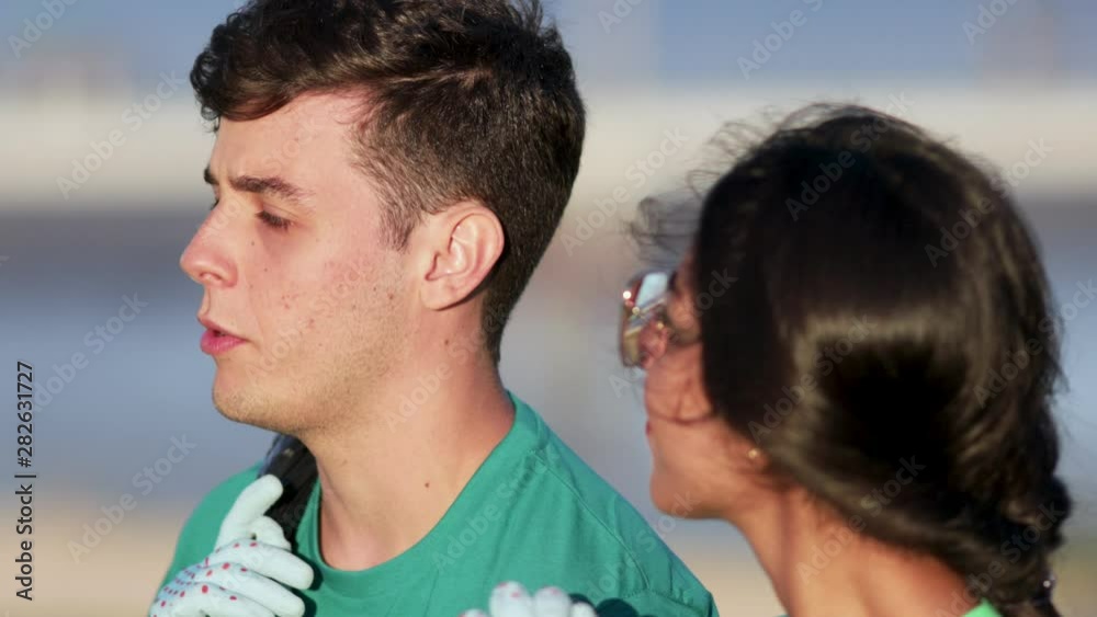 Cheerful volunteers talking outdoor. Close-up view of smiling young man and woman in green t-shirts holding garbage bags and talking in park. Volunteering concept Cheerful volunteers talking outdoor. Close-up view of smiling young man and woman in green t-shirts holding garbage bags and talking in park. Volunteering concept