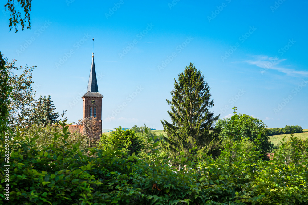tower of church between green trees, Hunspach, France tower of church between green trees, Hunspach, France