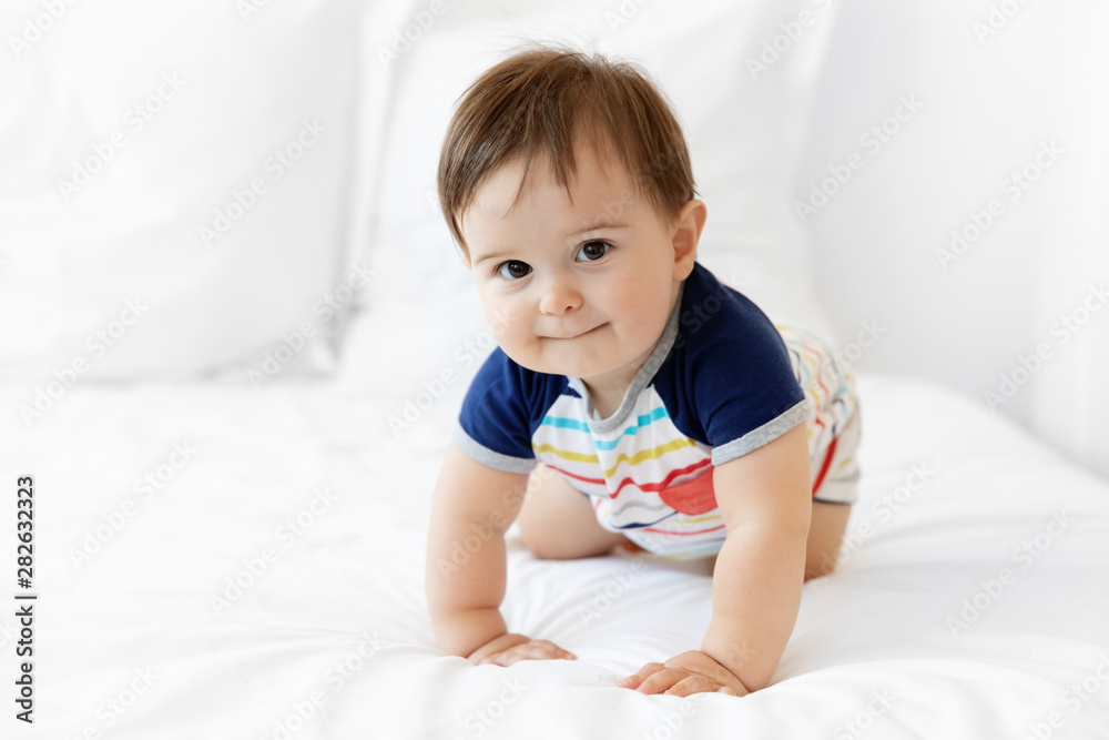 Cute baby crawling on white bed looking at camera Cute baby crawling on white bed looking at camera