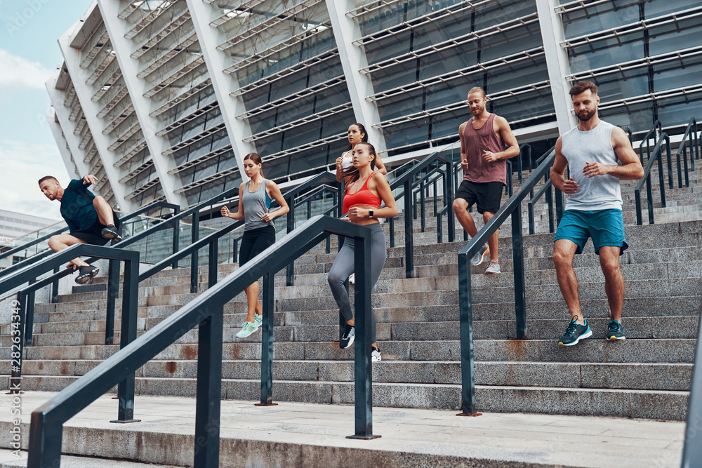 Group of young people in sports clothing jogging while exercising on the stairs outdoors