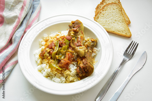 Chicken curry with rice one a white plate. Slices of bread, fork and knife.