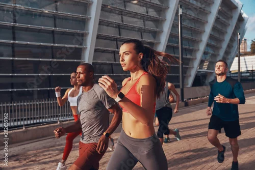 Obraz Group of young people in sports clothing jogging together outdoors