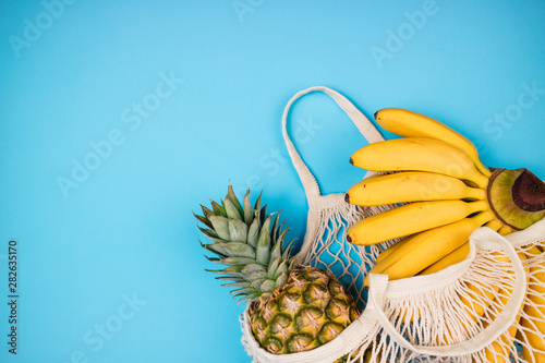 Fototapeta Naklejka Na Ścianę i Meble -  Shopping bag with organic banana and pineapple fruits on blue background. Shopping food with eco friendly bag. Caring for the environment, rejection of plastic, zero waste, recycling concept