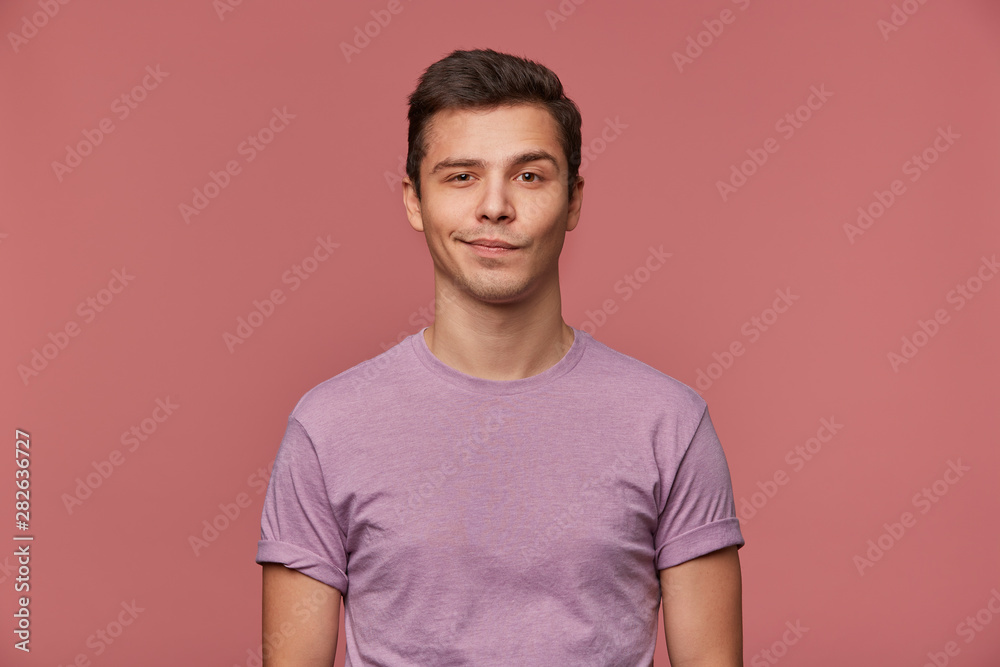 Portrait of handsome young man wears in blank t-shirt, looks at the camera with with a grin and happy expression, stands over pink background. Portrait of handsome young man wears in blank t-shirt, looks at the camera with with a grin and happy expression, stands over pink background.