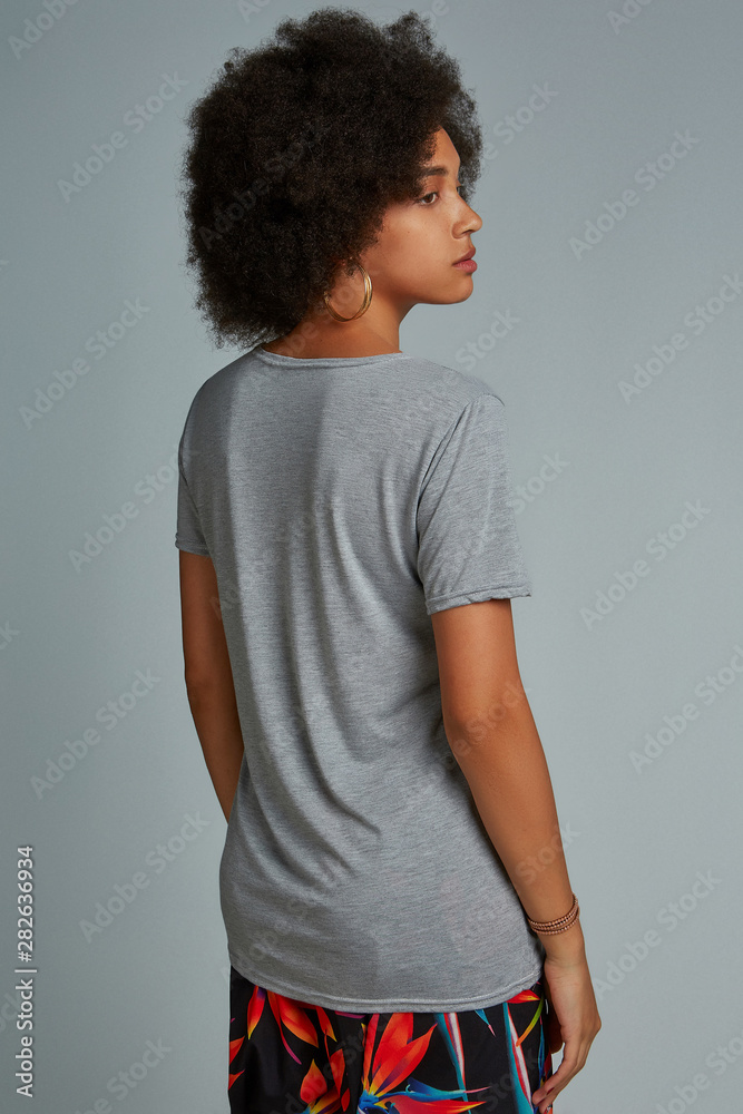 Half-turn back view photo of dark-skinned girl with afro hairstyle, wearing  grey t-shirt and colorful pants with floral print. She has big hoop  earrings and golden bracelet. Stock Photo | Adobe Stock
