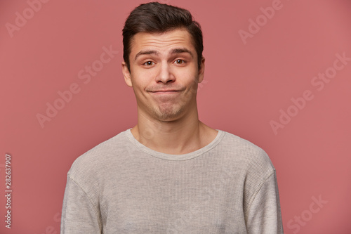 Portrait of handsome young sad man wears in blank t-shirt, looks at the camera with with mistrust, stands over pink background. © timtimphoto