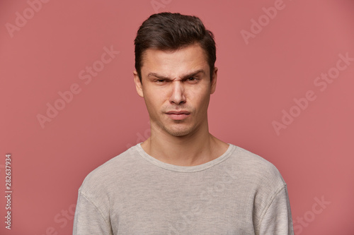 Close up of young handsome strict guy wears in basic long sleeve, looks at the camera with angry expression, isolated over pink background.