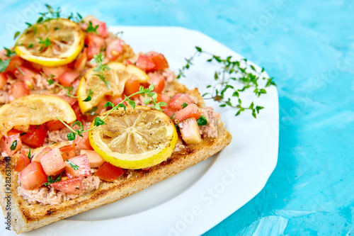 Appetizer bruschetta with tuna and tomatoes in white plate on blue background. Italian cuisine. Delicious Italian antipasti crostini. Copy space.