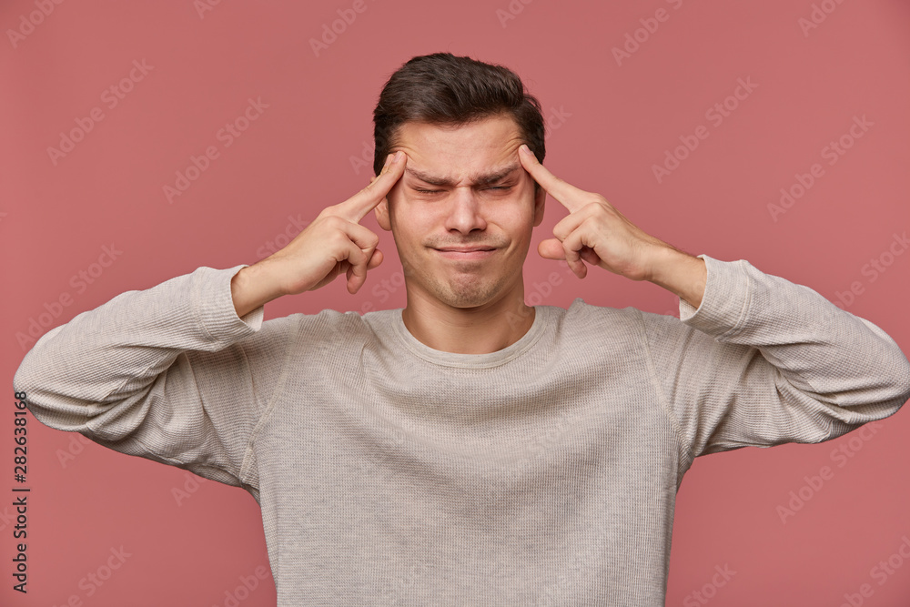 Photo of young attractive man in blank long sleeve, stands over pink background and shows headshot gesture with closed eyes, feels anhappy and migraineю Photo of young attractive man in blank long sleeve, stands over pink background and shows headshot gesture with closed eyes, feels anhappy and migraineю