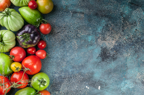 Tableau sur toile Different types, colors and shapes of tomatoes on a blue concrete background