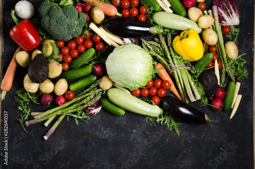 Top view portrait of Assortment of fresh raw vegetables on black wooden background with blank space.