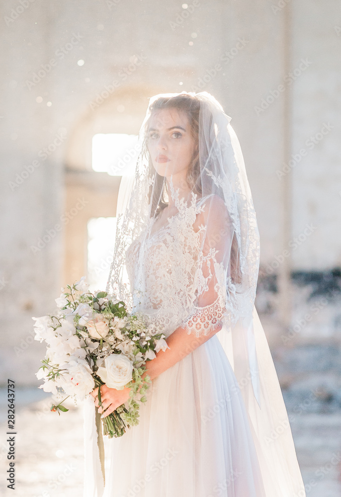 Portrait of pretty bride in luxury wedding dress with bouquet at the old cathedral. Bride posing near the place of the wedding ceremony.