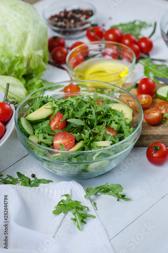 Fresh salad with cucumbers, cherry tomatoes, arugula, avocado, baby corn on white background. Vegetables on wood. Bio Healthy food, herbs and spices. Organic vegetables on wood.