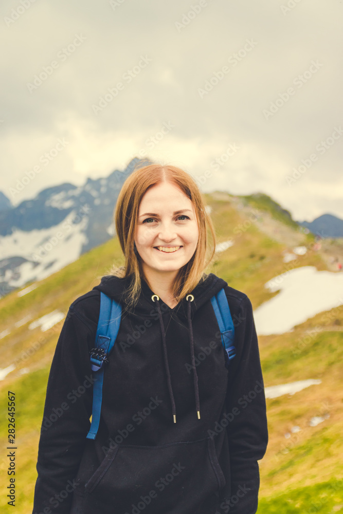 A cute blonde girl in a warm gray sweater climbed the peak of the mountain and looks at the photographer s camera.