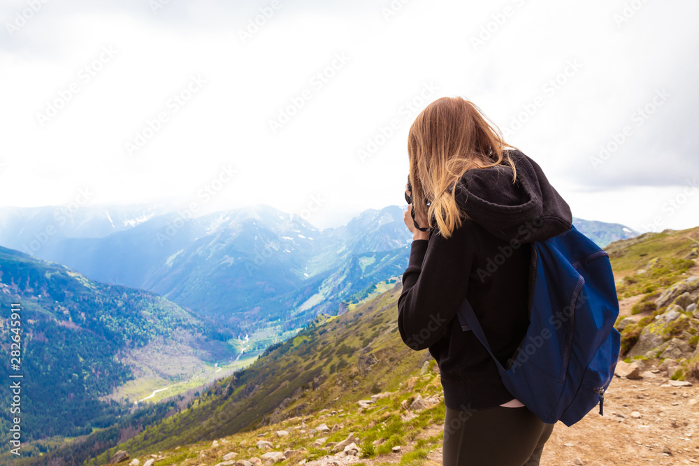 Young girl in a black sweater and leggings stands in the mountains and photographs the nature of beauty. Travel and blogging concept.
