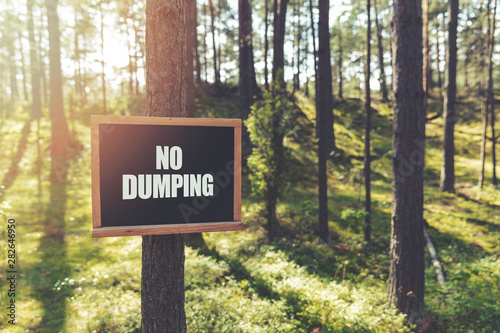 no dumping sign hanging on tree in forest