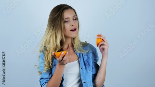 young beautiful sexy blonde woman licking one half of fresh orange on isolated white background