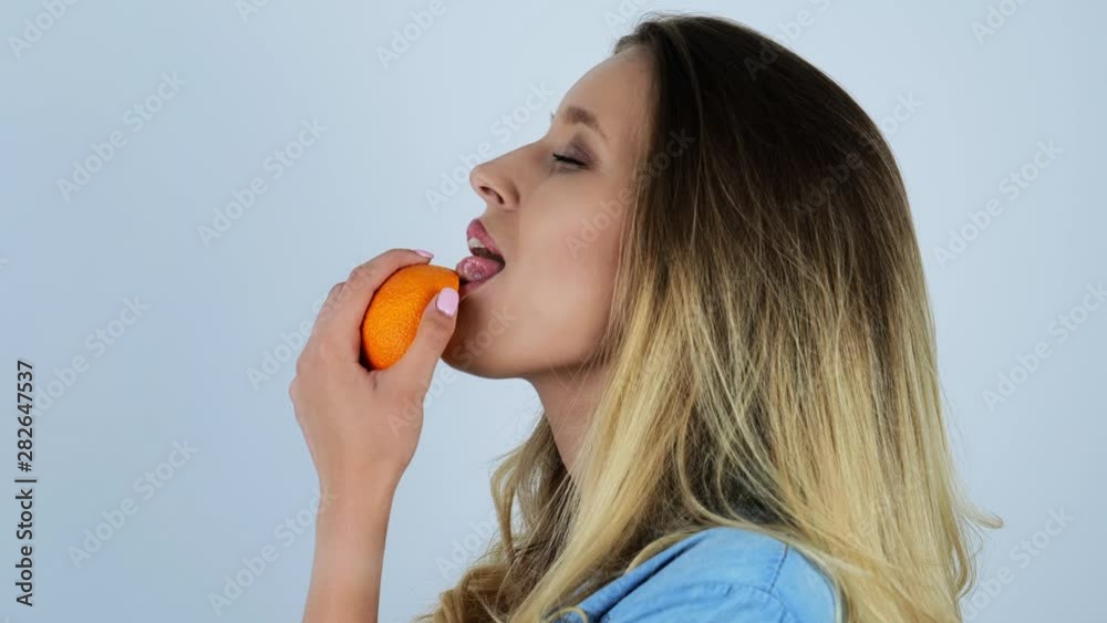 young beautiful sexy blonde woman licks half of fresh orange smiling on isolated white background young beautiful sexy blonde woman licks half of fresh orange smiling on isolated white background