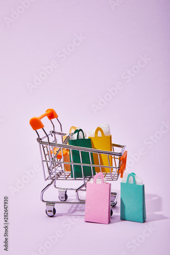 toy cart with colorful paper shopping bags on violet background