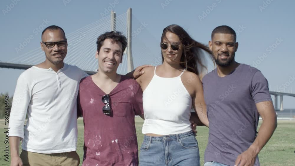 Front view of smiling friends hugging and walking on meadow. Happy group of people strolling during sunny day. Union concept Front view of smiling friends hugging and walking on meadow. Happy group of people strolling during sunny day. Union concept