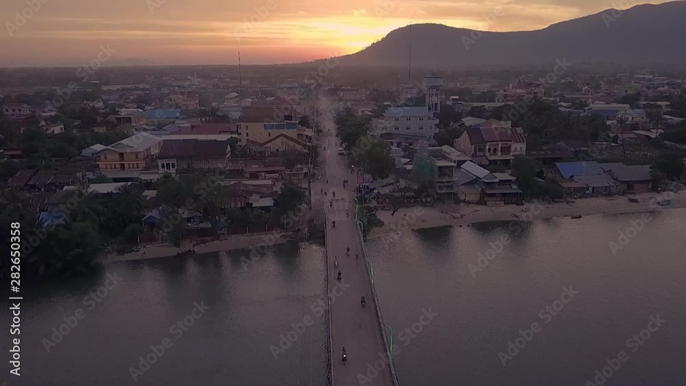 Overhead slowmotion video of motorbikes driving at sunrise over Entanou Bridge, which spans across the Praek Tuek Chhu river in Kampot, Cambodia