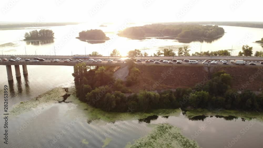 View from the drone to heavy traffic on a bridge over a river with a view of the islands in the distance. Backlight.