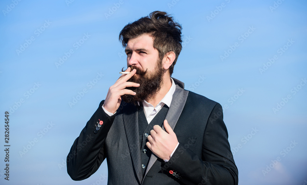 Guy with cigarette enjoy nicotine influence. Pleasure of smoking. Relaxing but harmful habit. Man with beard and mustache hold cigarette. Bearded hipster smoking cigarette blue sky background Guy with cigarette enjoy nicotine influence. Pleasure of smoking. Relaxing but harmful habit. Man with beard and mustache hold cigarette. Bearded hipster smoking cigarette blue sky background
