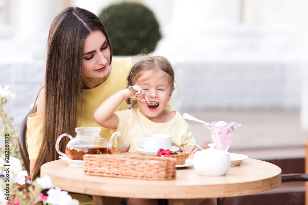 Beautiful mother sitting with child girl in cafe eating cake outdoors. Motherhood. Togetherness. Beautiful mother sitting with child girl in cafe eating cake outdoors. Motherhood. Togetherness.