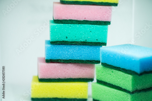 Different color sponges for washing dishes, staggered on top of each other close up on a white background