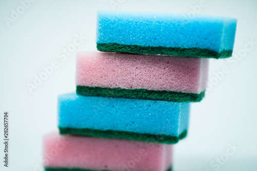 Different color sponges for washing dishes, staggered on top of each other close up on a white background
