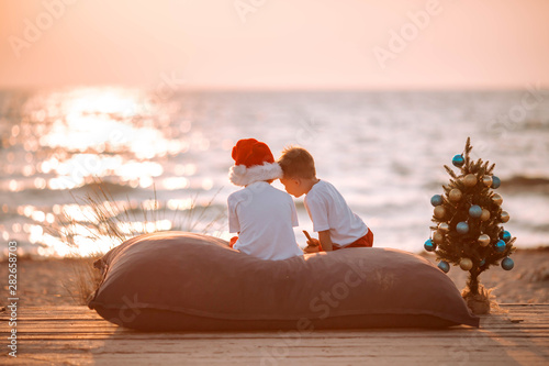 Two little boys on the beach at Christmas with a New Year tree.