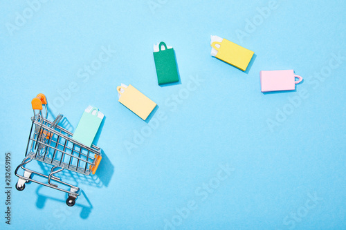 top view of toy shopping cart near colorful paper bags on blue