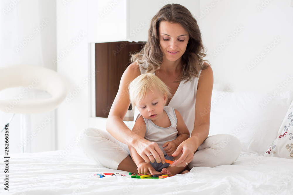 Mother plays with her toddler boy in bedroom with magnetic wooden blocks Mother plays with her toddler boy in bedroom with magnetic wooden blocks