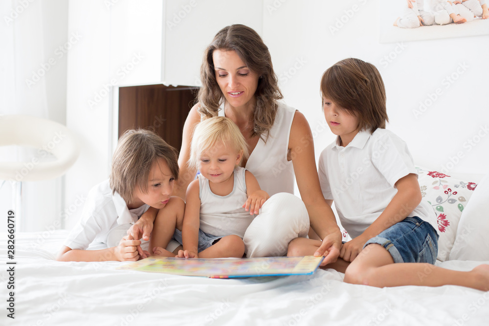 Young mother, read a book to her three children, boys, in the bed Young mother, read a book to her three children, boys, in the bed