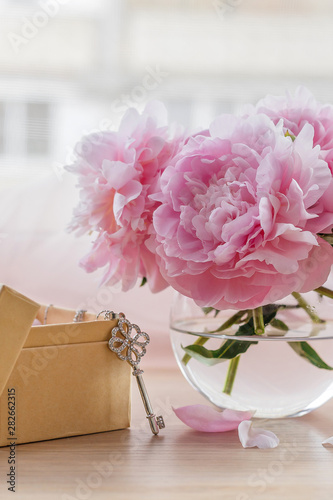 Still life with beautiful pink peonies in glass vase and little key