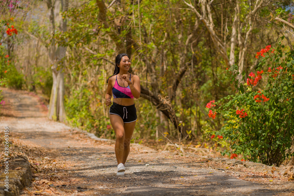 young happy attractive and exotic Asian Indonesian runner woman in jogging workout outdoors at countryside road track nature background running cheerful