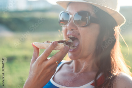 Beautiful middle aged woman bite a slice of pizza. Attractive woman eating pizza in sunset
