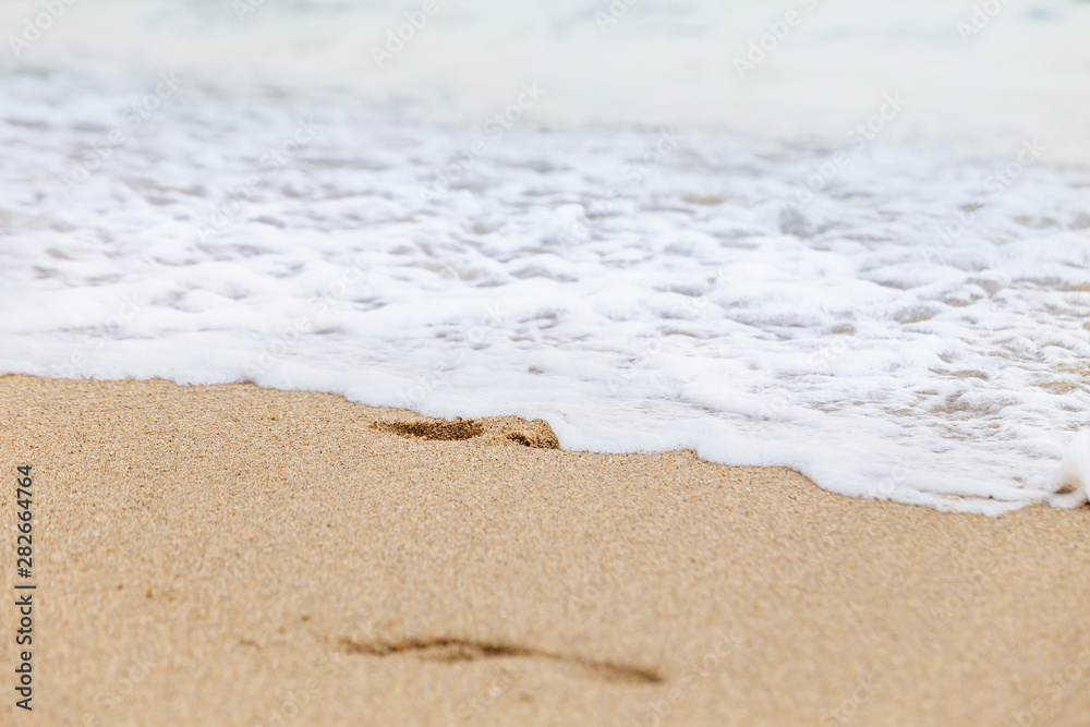 Footprints in the wet sand of the beach, washed away by the incoming sea wave.