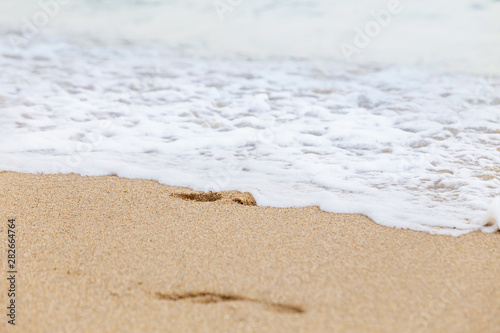 Fototapeta Naklejka Na Ścianę i Meble -  Footprints in the wet sand of the beach, washed away by the incoming sea wave.