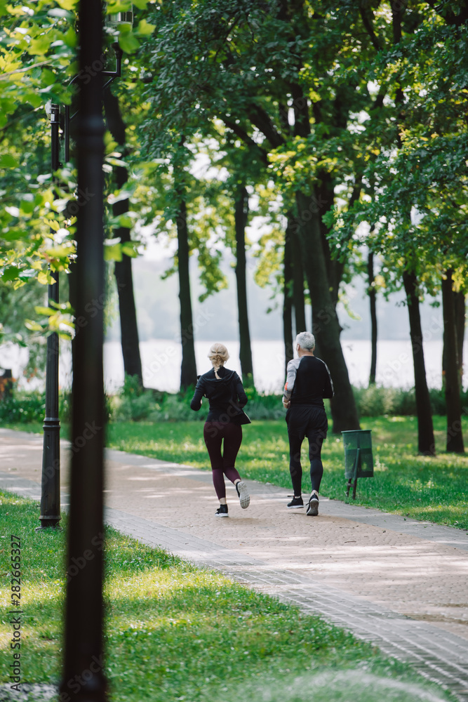 back view of mature sportsman and sportswoman running together in park