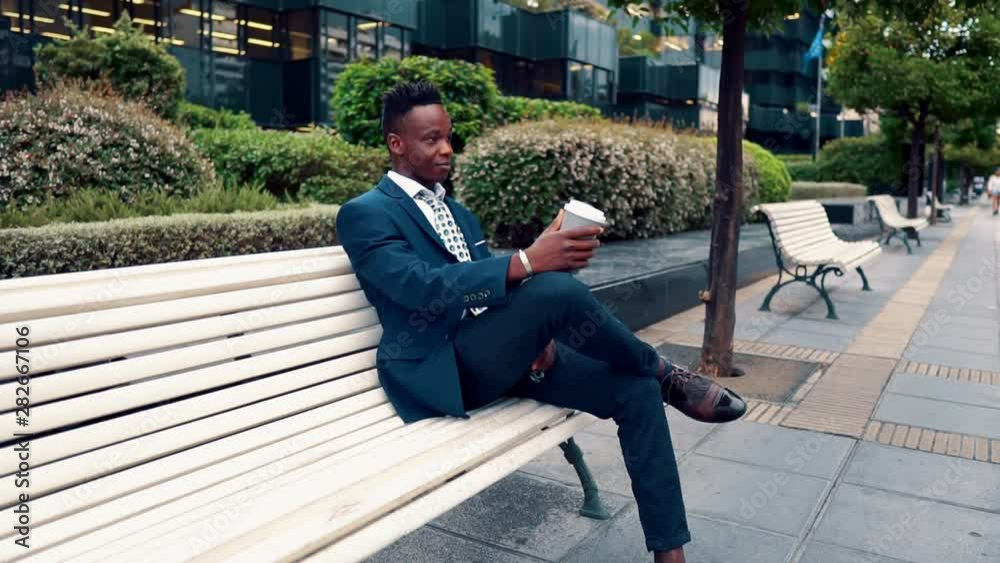 African American businessman wearing blue suit drinks coffee near office. Business concept African American businessman wearing blue suit drinks coffee near office. Business concept