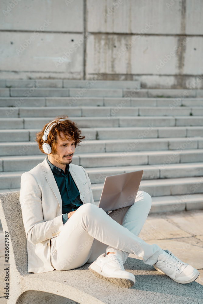 Businessman with headphones working on laptop outdoors Businessman with headphones working on laptop outdoors