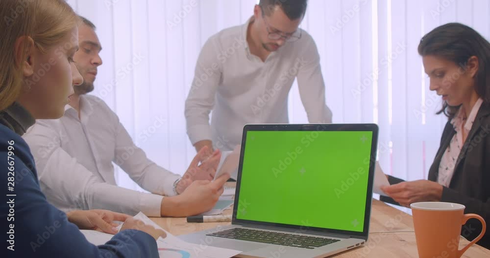 Portrait of four collleagues meeting in the office indoors. Business people using the laptop with green chroma key screen and having a discussion on the workplace Portrait of four collleagues meeting in the office indoors. Business people using the laptop with green chroma key screen and having a discussion on the workplace