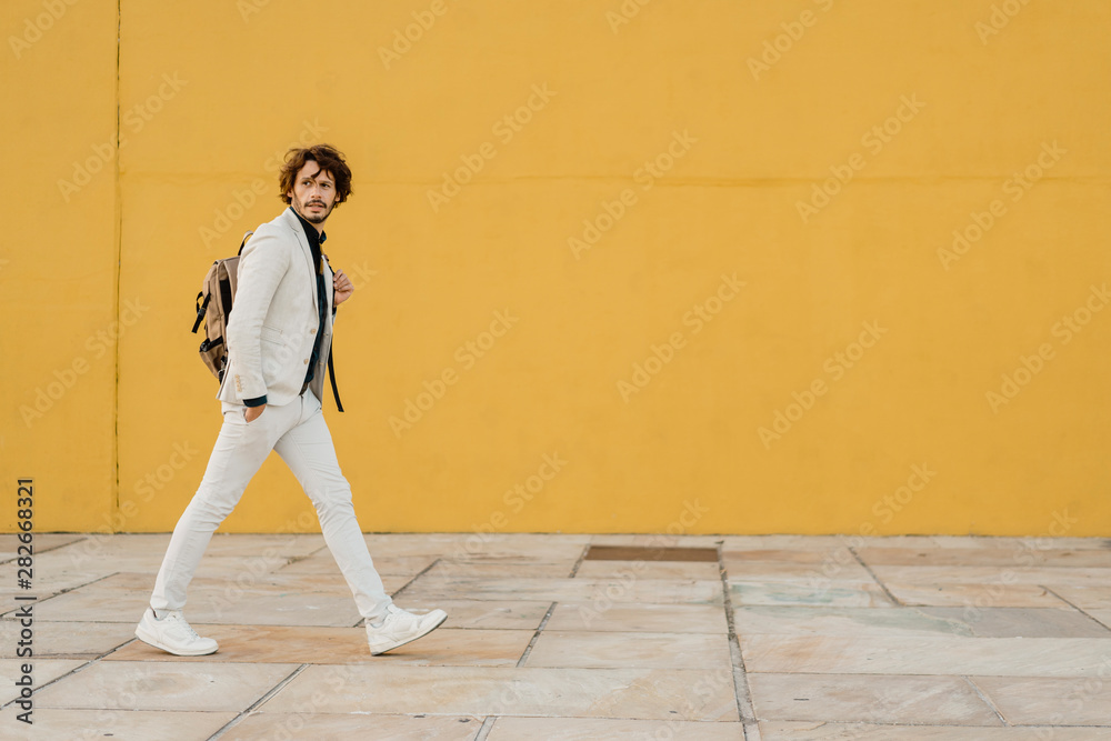 Portrait of walking businessman with backpack in front of yellow wall