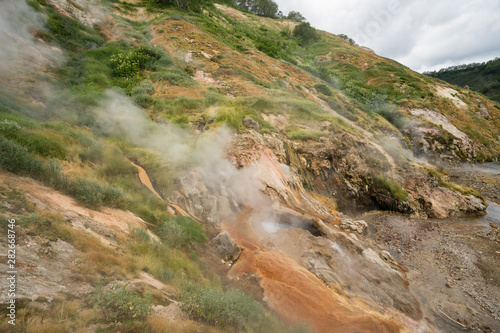 Geyser eruption in the Valley of Geysers in Kronotsky Nature Reserve, Kamchatka Peninsula, Russia. Colorful hill slope of Geysernaya River. Volcanic clay, and geothermal waters surrounding the scene.  photo