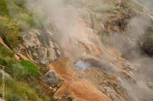 Geyser eruption in the Valley of Geysers in Kronotsky Nature Reserve, Kamchatka Peninsula, Russia. Colorful hill slope of Geysernaya River. Volcanic clay, and geothermal waters surrounding the scene.  photo