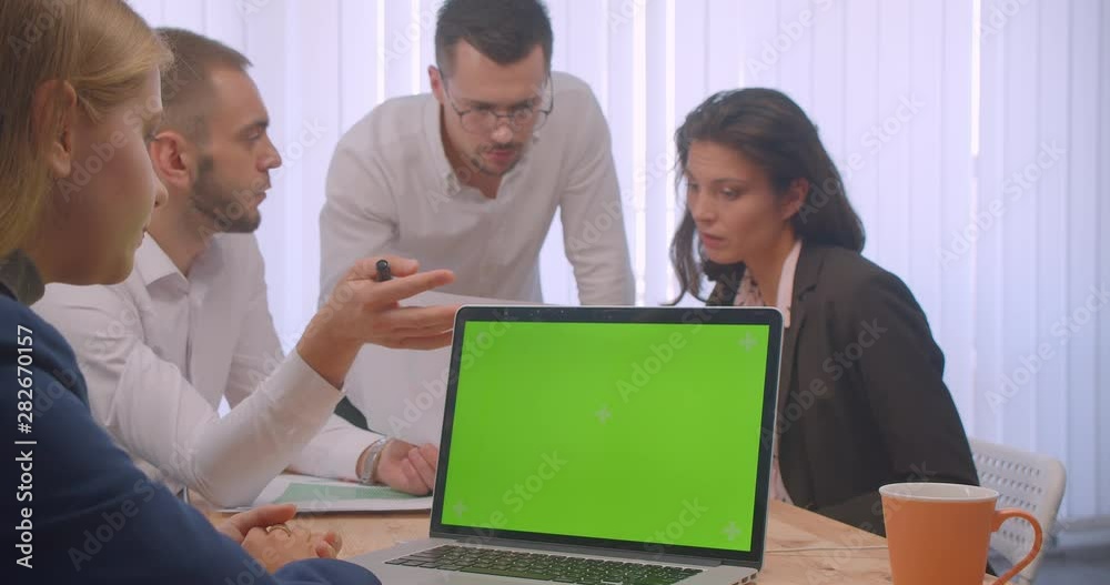 Portrait of four collleagues meeting in the office indoors. Business people using the laptop with green chroma key screen and having a discussion on workplace Portrait of four collleagues meeting in the office indoors. Business people using the laptop with green chroma key screen and having a discussion on workplace