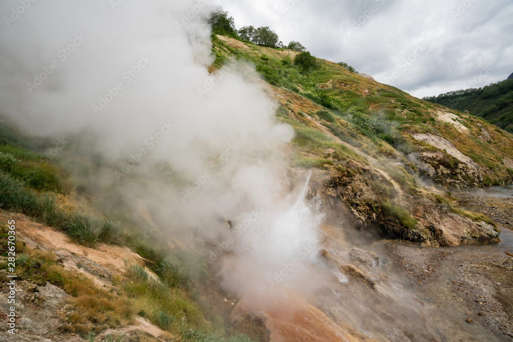 Geyser eruption in the Valley of Geysers in Kronotsky Nature Reserve, Kamchatka Peninsula, Russia. Colorful hill slope of Geysernaya River. Volcanic clay, and geothermal waters surrounding the scene. Geyser eruption in the Valley of Geysers in Kronotsky Nature Reserve, Kamchatka Peninsula, Russia. Colorful hill slope of Geysernaya River. Volcanic clay, and geothermal waters surrounding the scene.