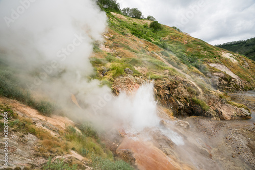 Geyser eruption in the Valley of Geysers in Kronotsky Nature Reserve  Kamchatka Peninsula  Russia. Colorful hill slope of Geysernaya River. Volcanic clay  and geothermal waters surrounding the scene. 