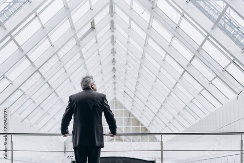 Serious elder man in big office centre thinking of future, investments and ideas. Shoot from the back